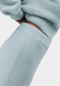 Světle modrý chlupatý pletený svetr má měkkou texturu a žebrované manžety, s viditelným švem po straně.