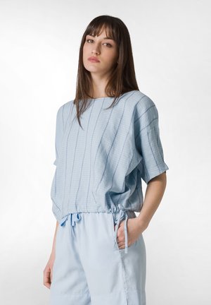 Maglietta azzurro chiaro a maniche corte con righe verticali e fondo con coulisse, abbinata a pantaloncini azzurro chiaro con tasche laterali.