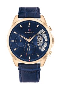 Orologio dorato con cinturino in pelle blu navy, quadrante blu, tre sottodial, indicatore della data e sezione trasparente che mostra il movimento.