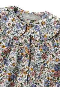 Blouse pour enfants avec col en forme de dentelle, boutons en bois et imprimé floral pastel en bleu, rose, jaune, blanc et vert sur tissu blanc.