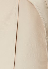 Tejido beige con una textura suave y un sutil brillo. Presenta costuras limpias y un detalle de diseño plegado a lo largo del borde.