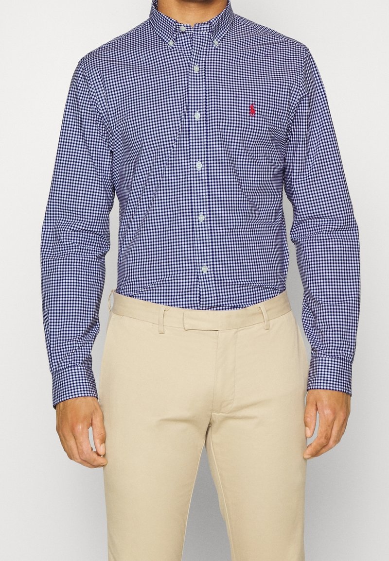 Košile s dlouhým rukávem v námořnické a bílé kostkované vzoru, vyrobená z bavlny, s límečkem a červeným logem na hrudní kapse.
