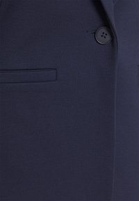 Knavblå kavaj i strukturerad tyg, med en enkel knappstängning och en fickdetalj med passpoal.