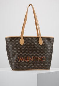 Smeđa torba s teksturiranim uzorkom Valentino logotipa, svijetlosmeđim ručkama i istaknutim narančastim "VALENTINO" na prednjoj strani.