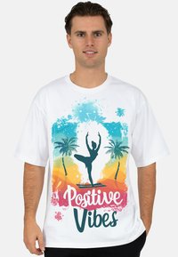 Wit T-shirt met een kleurrijk ontwerp van een danseressilhouet, palmbomen en de tekst "Positive Vibes" in roze en turkoois.