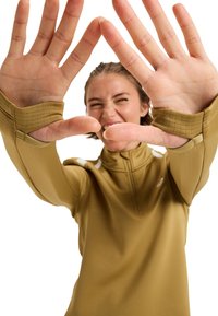 Langsleeve, ritssluiting top in olijfgroene stof met textuurpatroon, voorzien van duimopeningen en witte accenten op de schouders.