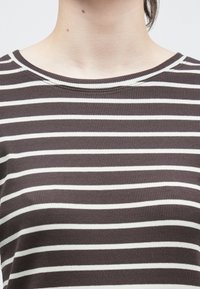 Pruunide ja valgete triipudega kootud t-särk soonilise tekstuuriga, ümara kaelusega ja lühikeste varrukatega.