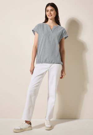 Blouse à manches courtes rayée avec un décolleté en V, présentant des lignes verticales bleues et blanches. Associée à un pantalon droit blanc et des baskets décontractées.