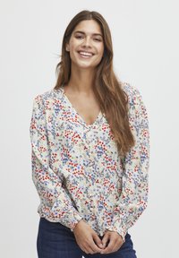 Camicia a maniche lunghe con bottoni in crema, caratterizzata da motivi floreali rossi e blu, maniche a sbuffo e scollatura a V. Tessuto strutturato.
