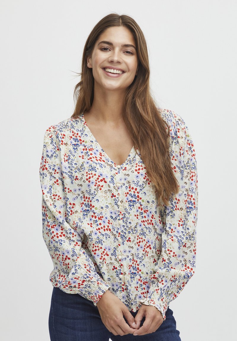 Camicia a maniche lunghe con bottoni in crema, caratterizzata da motivi floreali rossi e blu, maniche a sbuffo e scollatura a V. Tessuto strutturato.