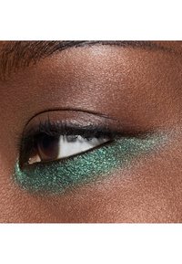 Eye close-up featuring a brown eyelid adorned with shimmering green eyeshadow, highlighting textured skin and defined eyelashes.