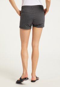 Harmaat puuvillahousut, joissa on taitetut lahkeet ja sileä pinta. Varustettu takataskuilla ja litteällä vyötäröllä, yhdistetty mustiin sandaaleihin.