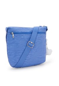 Modrá crossbody taška vyrobená z texturovaného nylonu, s uzávěrem na zip, nastavitelným popruhem a přívěskem ve tvaru pom-pomu připojeným k zipu.
