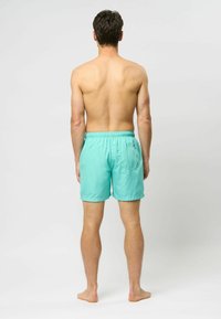 Türkiz fürdőshorts könnyű anyagból, rugalmas derekú és hátsó zsebbel, hátulról nézve.