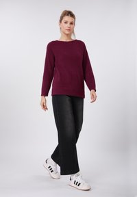 Pull bordeaux texturé à manches longues, col rond ; associé à un pantalon noir à jambes larges et des baskets blanches. Tenue simple et décontractée.