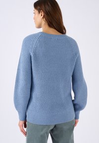 Lichtblauwe gebreide trui met een geribbelde textuur, lange opgeblazen mouwen en een ronde hals, gecombineerd met groene ribfluwelen broek.