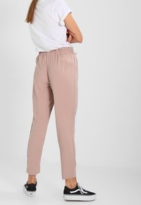 Vaaleanpunaiset, joustavavyötäröiset housut, jotka kapenevat lahkeista ja joissa on sivuraidat. Yhdistetty valkoiseen t-paitaan ja mustiin tennareihin. Sileä pinta.