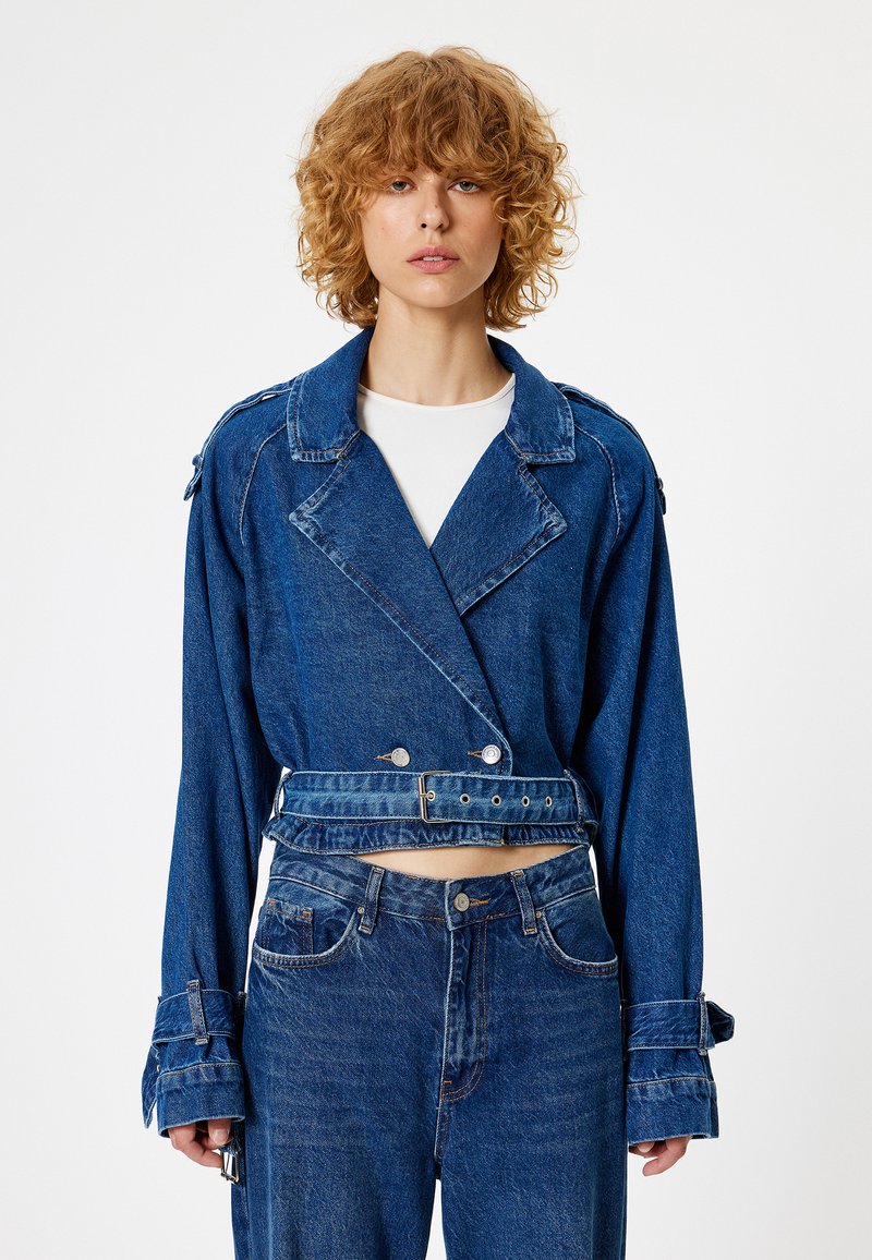 Chaqueta de mezclilla azul cortada, con bolsillos de parche, diseño de doble abotonadura, gran cuello y cintura con cinturón. Jeans de cintura alta a juego.