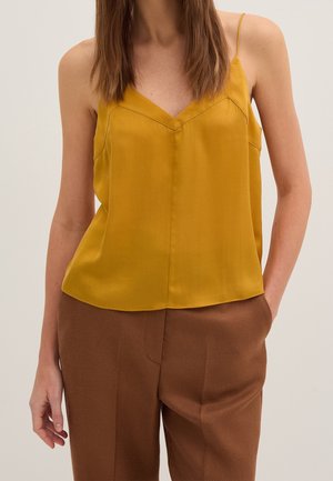 Sennepsgul satin camisole med tynde stropper, V-udskæring og diskret sømdetaljering; parret med strukturerede brune vidde bukser.