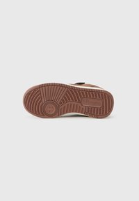 Talpa de sneaker din cauciuc cu un model texturat în nuanțe de maro. Prezintă un logo circular și zone întărite în jurul călcâiului și degetului mare.