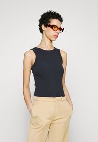 Svart ribbet tanktop med rund hals, kombinert med beige høyt liv bukser. Modellen har på seg vinklede røde solbriller.