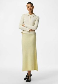 Crème geribbelde lange mouw polo-top met een kraag, gecombineerd met een gele, zacht aanvoelende lange rok. G gedragen met zwarte schoenen.
