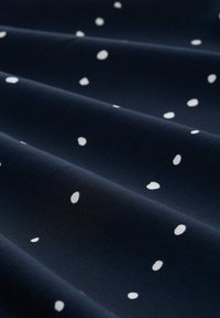 Navy Baumwollstoff mit einem Muster aus weißen, unregelmäßigen Punkten. Die Textur erscheint glatt mit sanften Drapierungen.