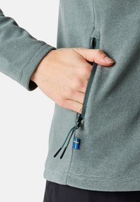 Light green sweater with textured fabric, featuring a side pocket and a drawstring with a small Swedish flag accent.