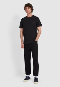 T-shirt nera in cotone a maniche corte e colletto rotondo, abbinata a pantaloni neri a gamba dritta e sneaker blu navy con suole bianche.