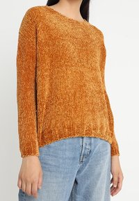 Pomarańczowy sweter o fakturowanej strukturze, z okrągłym dekoltem i długimi rękawami, z lekko skróconym dołem i miękkim, prążkowanym materiałem.