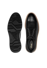Chaussures en cuir noir avec une texture lisse, présentant un design à lacets, un accent marron clair autour de la semelle, et une semelle en caoutchouc à motifs.