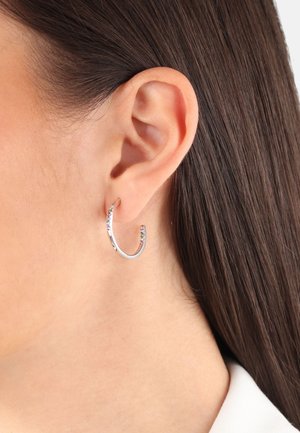 Pendientes de aro de plata con un diseño delgado y abierto que presenta pequeños y coloridos gemas a lo largo del borde. Acabado suave, ligero.