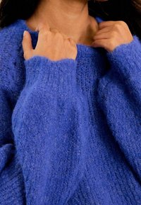 Pull oversize bleu profond en tissu tricoté texturé, avec poignets côtelés et col large. Apparence douce et confortable.