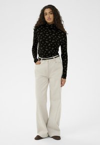 Čierny top s potlačou kvetín a rolákom, skombinovaný s béžovými širokými nohavicami, s hladkou textúrou a tenkým opaskom so zlatými kovovými prvkami.
