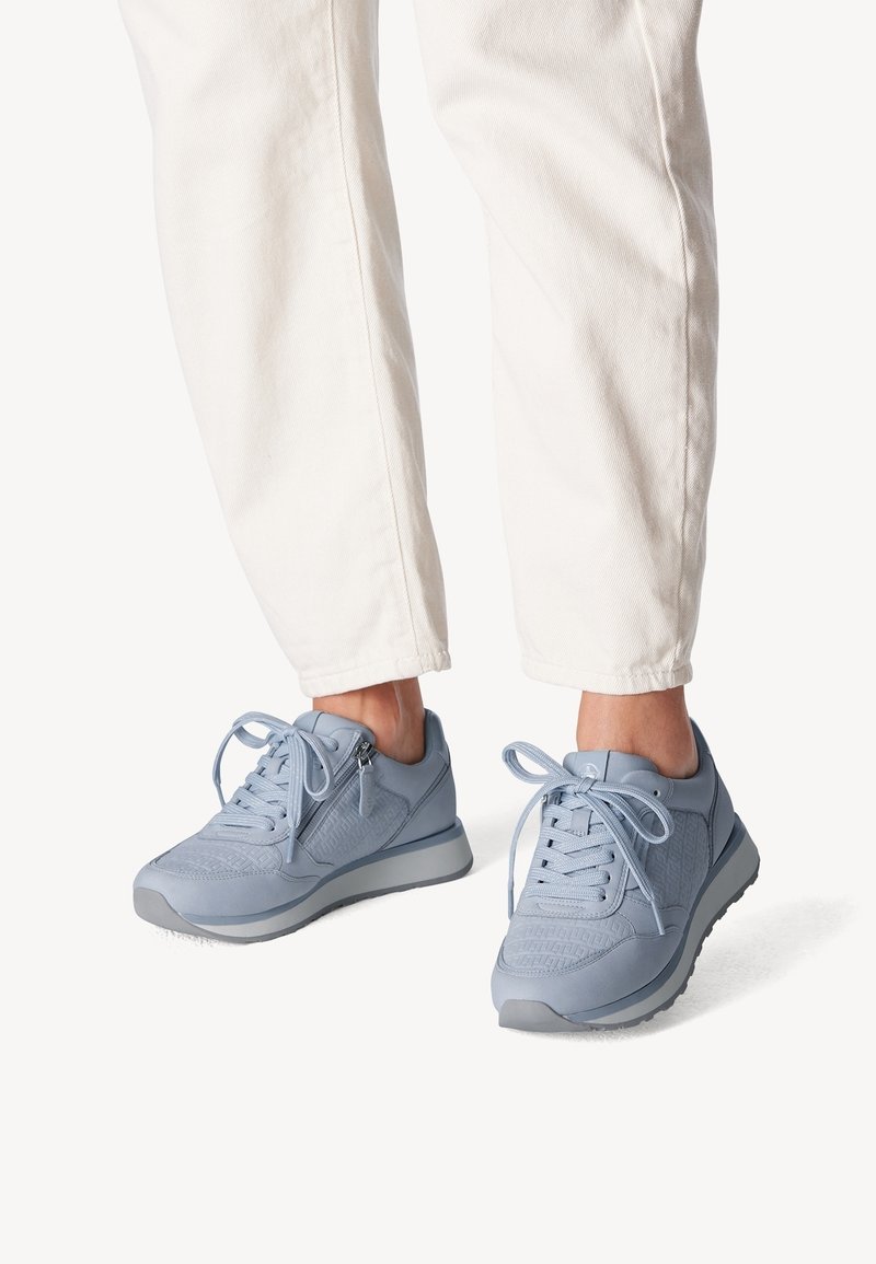 Vaaleansiniset urheilualueen kengät, joissa on verkkokangasta ja nahkaa, teksturoituja yksityiskohtia, pyöreä kärki, litteä pohja ja perinteinen nauhakiinnitys.