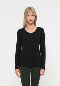 Must negra pikkade varrukatega keha lähedane topp, mis on valmistatud siledast kangast, ümmarguse kaelaaugu ja minimaalsete õmblustega, koos ribadega roheliste retuusidega.