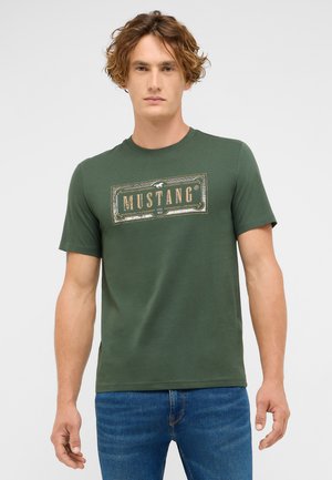 Green cotton t-shirt with a short sleeve design, featuring a rectangular "MUSTANG" logo in cream and dark green on the front.