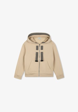 Haut à capuche beige zippé avec une doublure de capuche à motifs noir et blanc, deux poches avant et des sangles décoratives noires sur la poitrine.