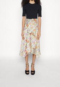 Haut noir à manches courtes associé à une jupe à volants imprimée de motifs floraux. La jupe présente des couleurs pastel et un nœud à la taille. Talons plateforme noirs.