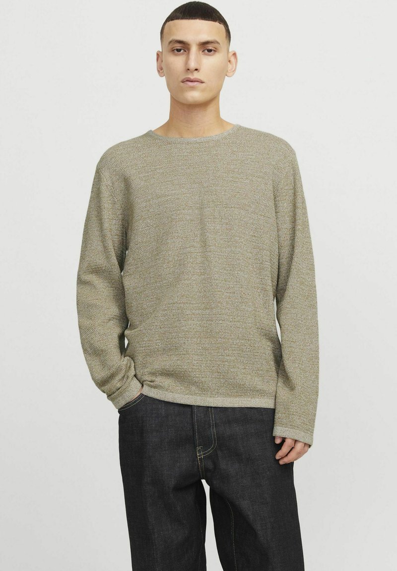 Khaki-langärmeliges Sweater mit strukturiertem Strickdesign, Rundhalsausschnitt und gerippten Bündchen, kombiniert mit dunkelblauen Jeans.