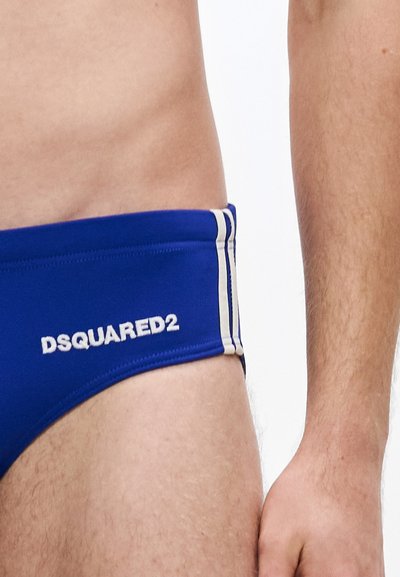Blaue Badehose mit glatter Textur, versehen mit weißem DSQUARED2-Logo und zwei weißen Streifen entlang der Seiten. Eng anliegendes Design.