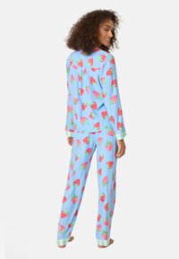Helles blaues Pyjama-Set mit einem Erdbeermuster. Langärmeliges Oberteil mit Knopfdetails und Hose mit gestreiften Bündchen an den Knöcheln.