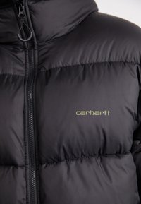 Schwarze Daunenjacke aus glattem, gesteppte Stoff, mit hohem Kragen, Reißverschluss und einem dezenten grünen "Carhartt"-Logo auf der Brust.