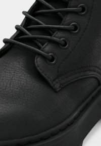 Black leather ankle boot with a textured finish, featuring black laces and eyelets. The sole has a slight elevation.