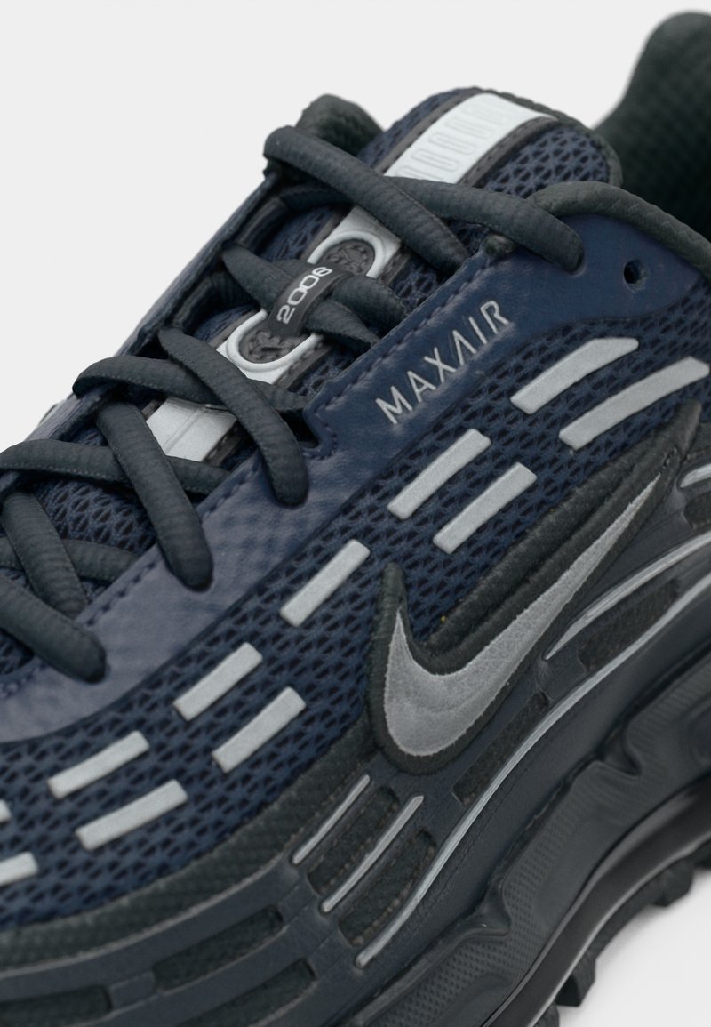 Detailaufnahme eines navy- und grau-farbenen Sportschuhs mit schwarzen Schnürsenkeln, versehen mit dem Text "MAX AIR" und dem grauen Nike-Swoosh an der Seite.