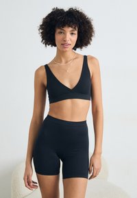 Black ribbed soft fabric bralette and high-waisted shorts set with a V-neck design, featuring wide straps and a smooth texture.