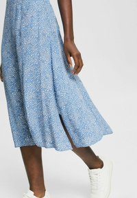 Abito midi blu con motivo a pois, orlo svasato e spacco laterale. Abbinato a sneakers bianche, che mettono in evidenza un tessuto leggero e morbido.