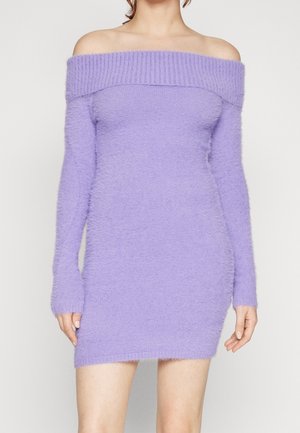 Woman wearing a fuzzy light purple off-shoulder long sleeve mini dress against a plain background.