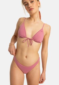 Ružový bikiny set pozostávajúci z trojuholníkového topu s nastaviteľnými šnúrkami a zodpovedajúcich nízko posadených nohavičiek, vyrobený zo jemného, elastického materiálu.