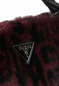 Tessuto peloso di un bordeaux scuro e nero con un logo triangolare in metallo nero di Guess USA attaccato vicino al bordo superiore.